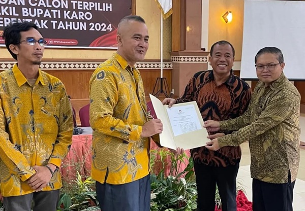 Ketua KPU Karo Rendra Gaulle Ginting menyerahkan hasil SK rekapitulasi kepada pasangan Antonius Ginting dan Komando Tarigan terpilih sebagai Bupati-Wakil Bupati Karo dalam Pemilkada 2024. Foto Rienews.com.